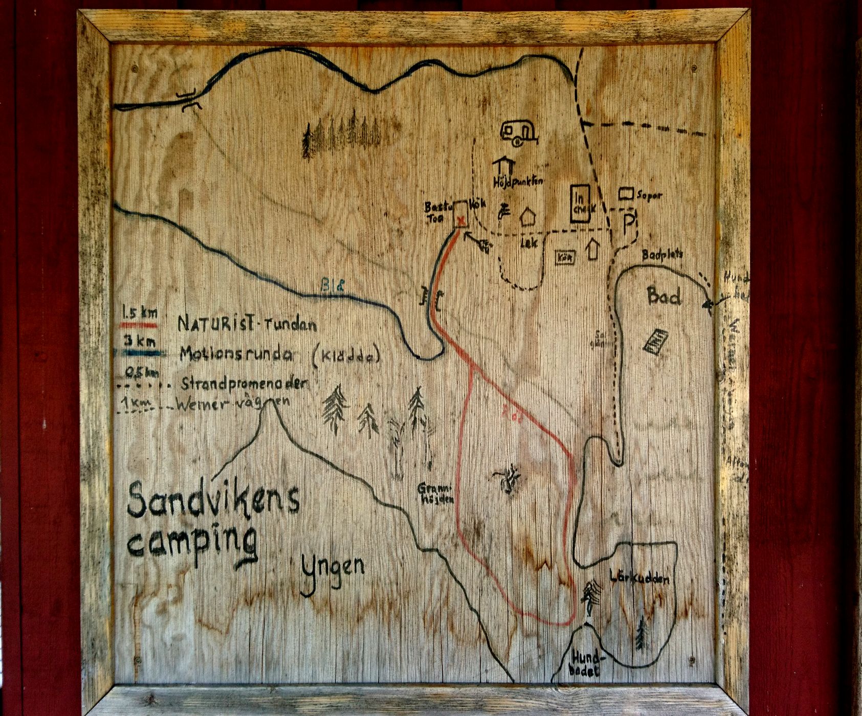 Der Plan des Camps auf Holz gemalt hängt an einer Hauswand im typischen Rot der schwedischen Holzhäuser. Die „Motionsrunda“ (Bewegungsrunde) soll man in Klädda (Kleidern) absolvieren (1/15)